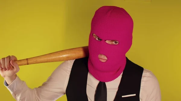 Homme en cagoule rose avec batte de baseball. Hooligan en masque avec batte dans les mains. Un homme dans une entreprise costume élégant strict avec une chauve-souris en bois dans ses mains — Photo