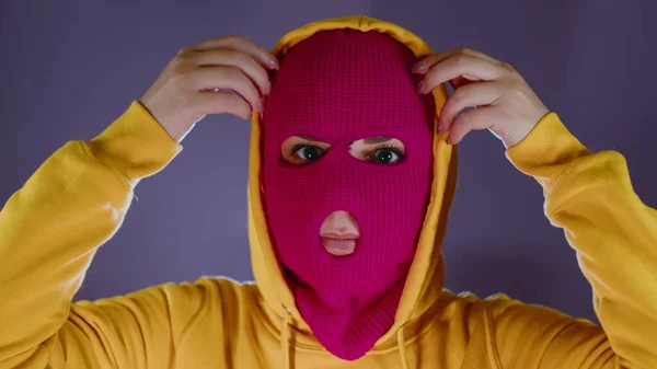 Młoda kobieta w różowej kominiarce zdejmuje kaptur. Hooligan w masce zdejmuje kaptur z kapturem, patrząc w kamerę. — Zdjęcie stockowe