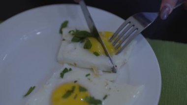 Beyaz tabakta maydanozlu sahanda yumurta. Tanınmayan bir kadın parçayı keser ve yer. Kahvaltı konsepti.