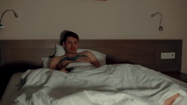 Genç adam yatakta battaniyenin altında yastığa uzanıyor ve akşam geç saatlerde televizyon seyrediyor. Rahat erkek şovlar izler, uzaktan kumandayla televizyonu kapatır ve karanlık odada gözlerini kapatır..