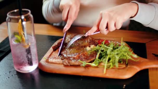 Filete suculento con verduras sobre tabla de madera. Mujer irreconocible corta la pieza y come. Concepto alimenticio. — Vídeos de Stock