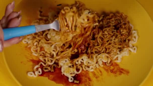 Ready-made instant noodles with condiment and spicy sauce in yellow plate on yellow background. Unrecognizable person with fork shuffles ramen with additives. Close up. — Stock Video