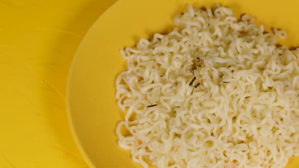 Fideos instantáneos listos en placa amarilla sobre fondo amarillo. Persona irreconocible rocía condimento picante en el plato con ramen. De cerca.. — Vídeos de Stock