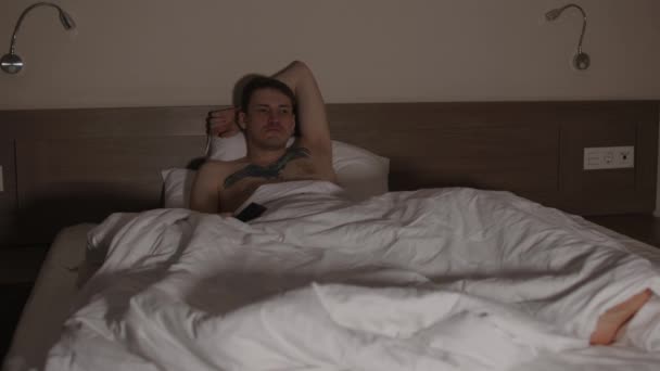 Giovane uomo sdraiato sul cuscino sotto la coperta a letto e guardando la TV a tarda sera. Rilassato maschio programmi di visione di show e switch canale con telecomando in camera oscura. — Video Stock