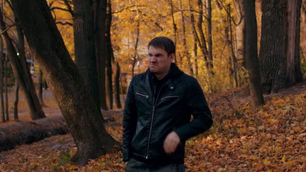 Un jeune homme pète dans la forêt d'automne. Le feutre masculin détendu pue, regarde autour de lui et part. Mouvement lent. — Video