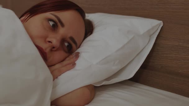 Ung kvinde ligger på puden under tæppe og kigger væk. Tankevækkende kvinde hviler i sengen i weekenden. – Stock-video
