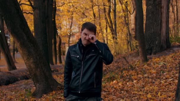 O jovem esfrega os olhos na floresta de outono. masculino fricção olhos de fadiga enquanto pé no cidade parque. — Vídeo de Stock