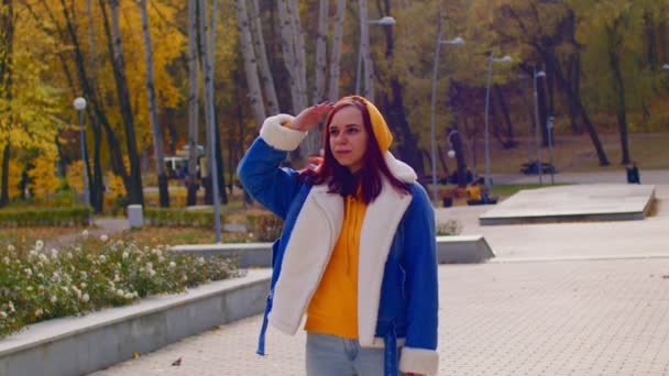 Een jonge vrouw die in de verte kijkt en haar hand boven ogen houdt in het stadspark. mooi vrouw in casual kleding kijken weg en peering. — Stockvideo