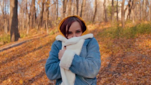 Νεαρή παγωμένη γυναίκα με ζεστό τζιν μπουφάν. Όμορφη γυναίκα τυλιγμένη σε γούνινο μπουφάν που κρέμεται από το κρύο, ενώ στέκεται στο δάσος του φθινοπώρου. — Αρχείο Βίντεο
