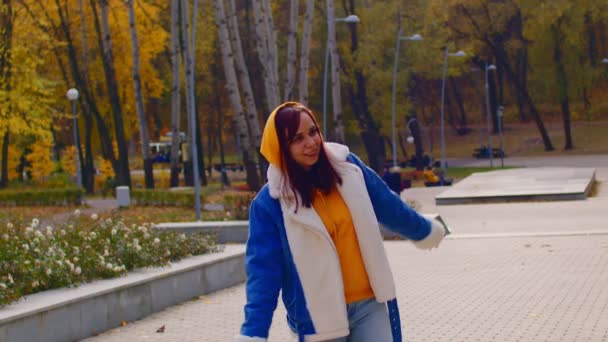 Mujer joven bailando en el parque. Hermosa hembra en ropa casual sonríe y se alegra del buen tiempo en la temporada de otoño. Movimiento lento. — Vídeos de Stock