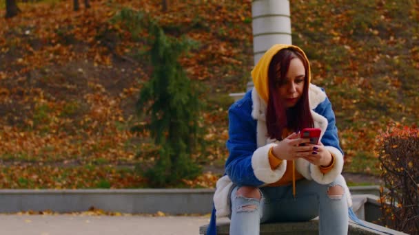 Jonge vrouw met mobiele telefoon in het stadspark. Mooie vrouw in casual kleding browsen smartphone tijdens het rusten op wandeling. — Stockvideo