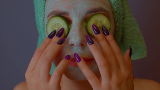 Kobieta w masce na twarzy trzyma plastry ogórka na oczach. Zrelaksowana pani dbająca o twarz maską kosmetyczną i świeżymi warzywami. Pojęcie spa, pielęgnacji skóry i naturalnego piękna w warunkach domowych. — Wideo stockowe
