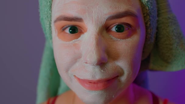 Mujer joven con toalla en la cabeza y máscara en la cara después de los procedimientos de ducha. Señora cortejo de su cara con máscara cosmética facial. Concepto de spa, cuidado de la piel y belleza natural en condiciones domésticas. — Vídeo de stock