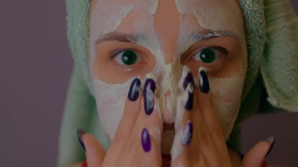 Young woman with towel on head applies mask on face after shower procedures. Lady courting of her face with facial cosmetic mask. Concept of spa, skincare and natural beauty in domestic conditions. — Stock Video