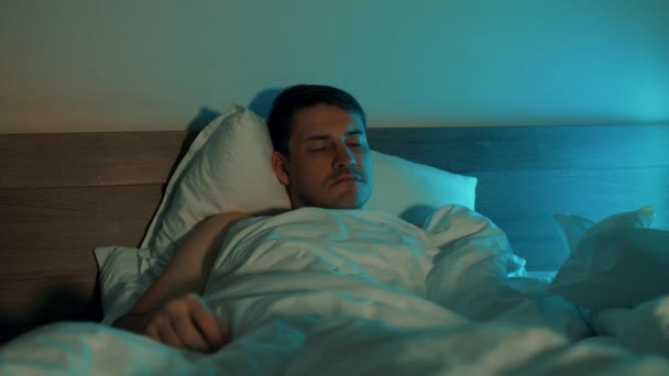 Unge man ligger på kudden under filten och sover på sängen. Sömnig man vaknar, tittar på tiden i mobilen och nervös som försov. — Stockvideo