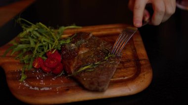 Tahta tahtada sebzeli leziz biftek. Tanınmayan bir adam parçayı keser ve yer. Yiyecek konsepti.