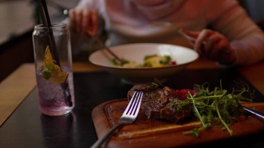 Tahta tahtada sebzeli leziz bifteğin seçici odağı. Tanımlanamayan kadın arka plandaki restoranda yemek yiyor. Kapat..