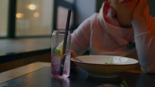 Selektiver Schwerpunkt des erfrischenden Erfrischungsgetränks auf dem Tisch. Unerkennbare Frau isst Gericht im Restaurant im Hintergrund. Nahaufnahme. — Stockfoto