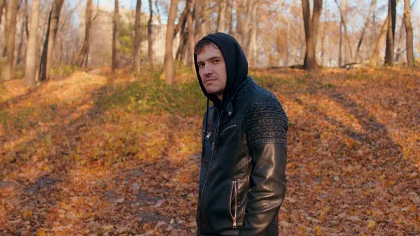 Young man in autumn forest. Male turns his head, looks at camera and smiles while standing in city park. — Stock Photo, Image