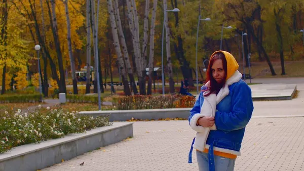 Giovane donna morde le labbra, guardando la fotocamera. Donna offesa in abiti casual in piedi nel parco della città. — Foto Stock