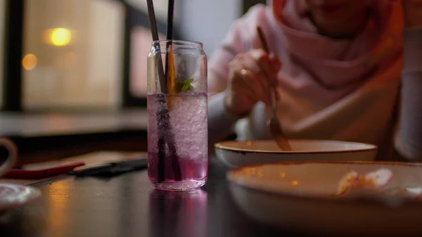 Selektiver Schwerpunkt des erfrischenden Erfrischungsgetränks auf dem Tisch. Unerkennbare Frau isst Gericht im Restaurant im Hintergrund. Nahaufnahme. — Stockfoto