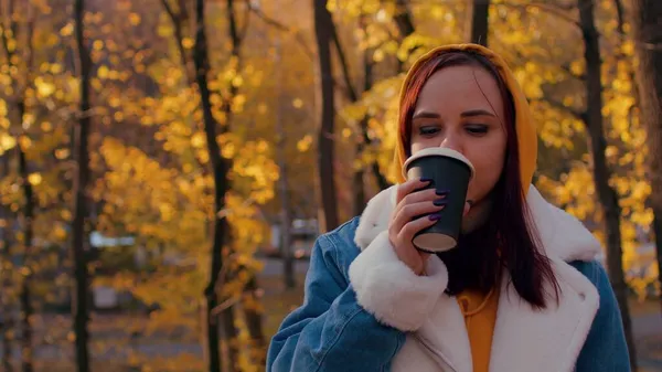 Egy fiatal nő kávét iszik az őszi erdőben. Gyönyörű nő alkalmi ruhák élvezi forró ital papír pohár álló napos szezonális erdőben. — Stock Fotó