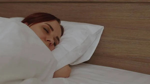 朝、毛布の下で寝ている若い女性。寝たきりの女が目を覚ますと、枕の上に横になって. — ストック写真