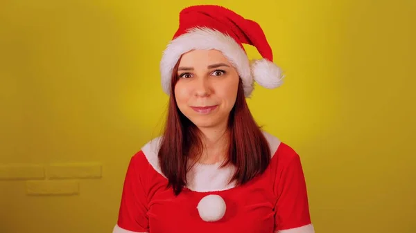 Mujer en traje de santa guiños sobre fondo amarillo. Bonita hembra en sombrero de Navidad coqueteando y mirando a la cámara. — Foto de Stock