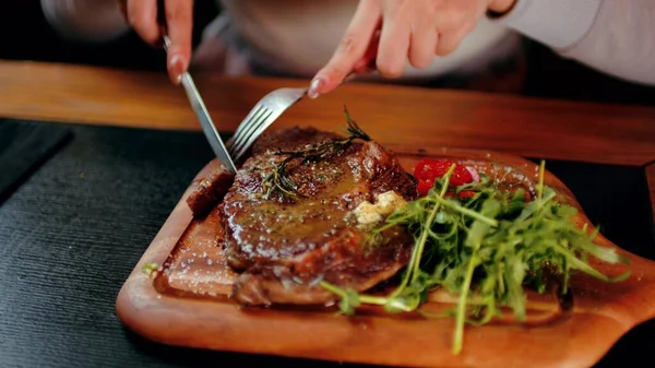 Sappige biefstuk met groenten op houten plank. Onherkenbare vrouw snijdt het stuk af en eet. Voedselconcept. Stockfoto