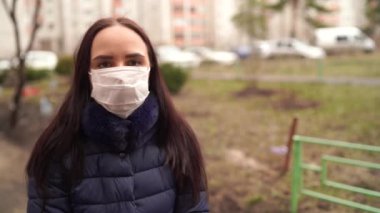 Sokakta avluda yüzünde tıbbi maske takan genç bir kadının portresi. Yetişkin kadın kendini hastalıklardan korumak için yüzünü maskeyle örttü..