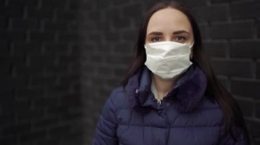 Yüzünde siyah tuğla duvara dayalı tıbbi maske takan genç bir kadın portresi. Yetişkin kadın kendini hastalıklardan korumak için yüzünü maskeyle örttü..