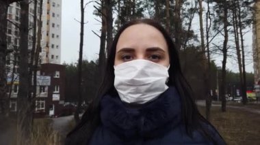 Sokakta avluda yüzünde tıbbi maske takan genç bir kadının portresi. Yetişkin kadın kendini hastalıklardan korumak için yüzünü maskeyle örttü..