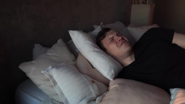 若い男は早朝に枕の上で寝ていた 怒り狂った男は睡眠を妨げる騒音のために枕で頭を覆う — ストック動画
