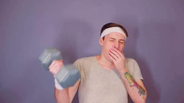 Man in sports headband yawns and lifts dumbbell. Tired male doing sport and wants to sleep. — Stock Video