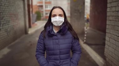 Yüzünde tıbbi maske takan, sokakta kemerde duran genç bir kadının portresi. Yetişkin kadın kendini hastalıklardan korumak için yüzünü maskeyle örttü..
