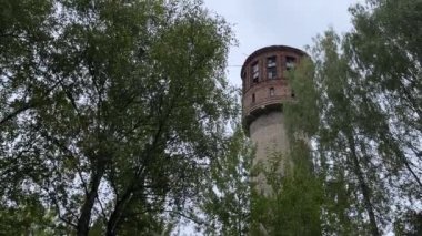 Ağaçlarla çevrili eski yüksek su kulesi. Taşrada tuğla kule.