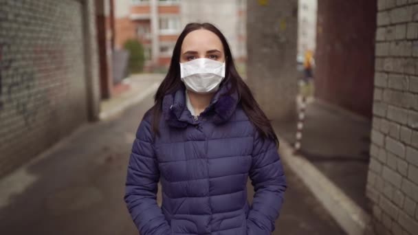 路上のアーチに立って 彼女の顔に医療用マスクの若い女性の肖像画 大人の女性は病気から身を守るためにマスクで顔を覆いました — ストック動画