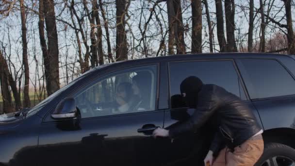 Хулиган в маске с бейсбольной битой подкрадывается к машине, открывает дверь и бьет битой. Водитель направил пистолет на бандита, и он сдался. Концепция защиты и самообороны. — стоковое видео