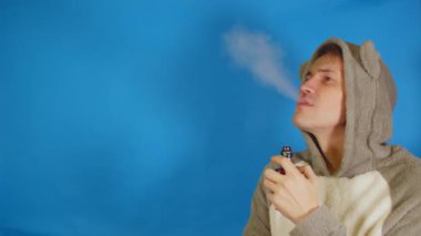 Kapüşonlu bir adam, kulakları kulaklıklı, gözlerini kaçıran, mavi arka planda duran, yazı için yeri olan. Erkek, yelesinden buhar çıkarır..