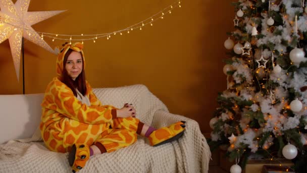 Женщина Костюме Жирафа Сидит Диване Канун Рождества Улыбающаяся Молодая Женщина — стоковое видео