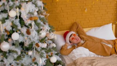 Noel Baba şapkalı ve güneş gözlüklü bir adam Noel ağacının yanında yatıyordu. Yeni yıl atmosferinde dinlenen şık erkek kapalı mekanlarda tatil yapıyor..