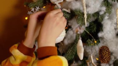 Tanınmayan kişi Noel ağacını süslüyor. Evde Noel kutlaması için hazırlanırken kadınların elleri köknar dalına parlak süslemeler asıyor. Kapat..