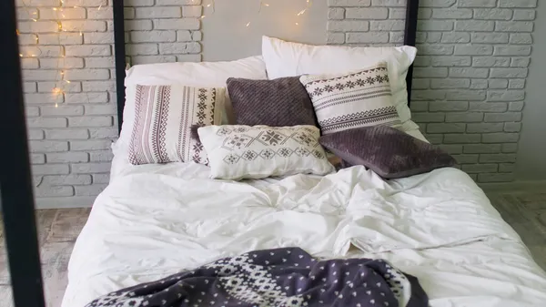 Большая кровать с подушками и одеялами внутри. Светящаяся гирлянда над кроватью. Интерьер комнаты в студии. — стоковое фото