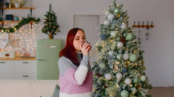 Jeune femme buvant des boissons et dansant près de l'arbre de Noël dans le salon. Femme divertissant avec un verre d'alcool pendant les fêtes. — Photo