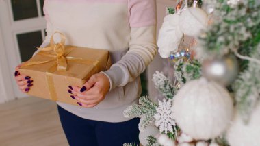Elinde hediye kutusu tutan tanınmayan biri. Noel ağacının yanında elinde Noel hediyesi olan kadınların elleri. Kapatın. Tatillerde sürpriz kavramı.