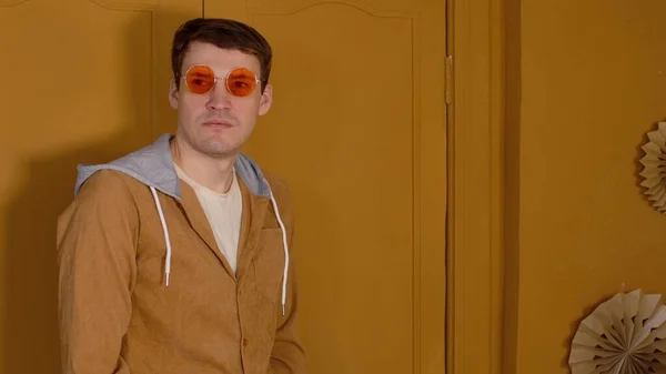 Jeune homme beau dans des lunettes debout sur fond de portes brunes dans la chambre. Portrait de mâle élégant regardant loin. — Photo