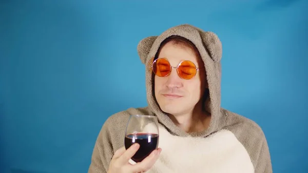 Homme en lunettes de soleil et sweat à capuche avec oreilles sent l'arôme de vin rouge sur fond bleu. Homme élégant appréciant le parfum de l'alcool. — Photo