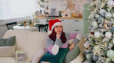 Noel Baba şapkalı ve örgü kazaklı kafası karışmış bir kadın oturma odasındaki Noel ağacının yanındaki koltukta oturuyor. Düşünceli bir kadın çenesini kaşıyor ve şüpheyle kameraya bakıyor..