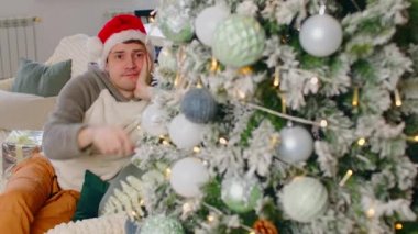 Noel Baba şapkalı bir adam kanepeye oturup Noel ağacına bakıyor. Mutsuz erkek, bayramları kutlarken Noel ağacı süslemelerini düşünür ve ona dokunur..
