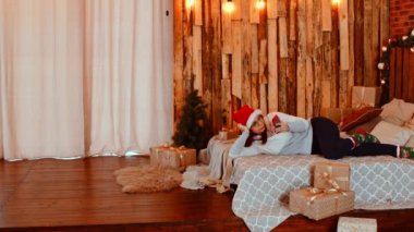 Noel Baba şapkalı genç bir kadın akıllı telefona bakıyor, yatakta yatıyor. Güzel bir bayan cep telefonuyla dinleniyor ve Noel 'i evde kutluyor. Tatil anlayışı ve iyi ruh hali.